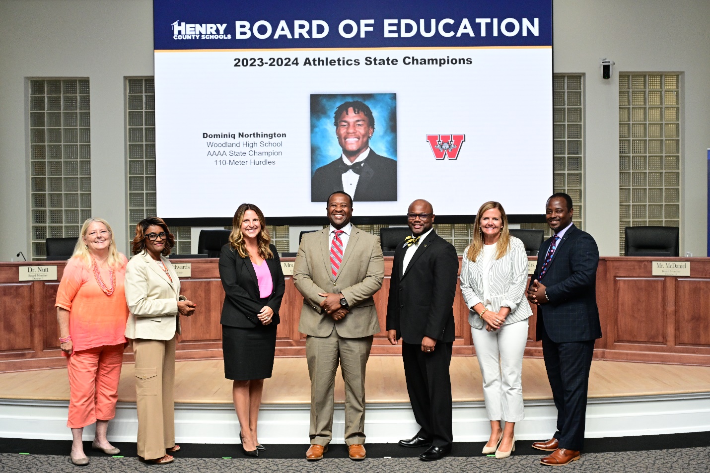 A group of people standing in front of a large screenDescription automatically generated